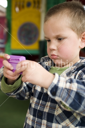 A young boy plays with a digital toy in front of playground