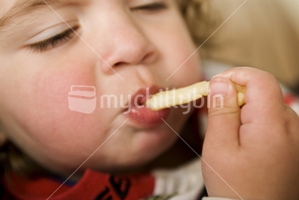 A sleepy young toddler eats a french-fry