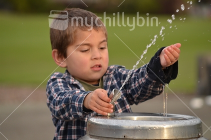 A boy sprays water from a drinking fountain