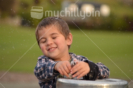 Boy being a boy; sprays himself with water at a drinking fountain.