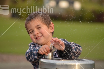 Boy sprays himself with water at a drinking fountain