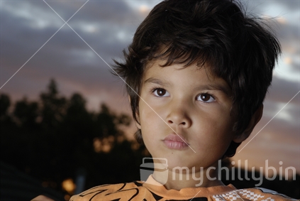 A New Zealand Maori boy with serious expression on a sunset backdrop