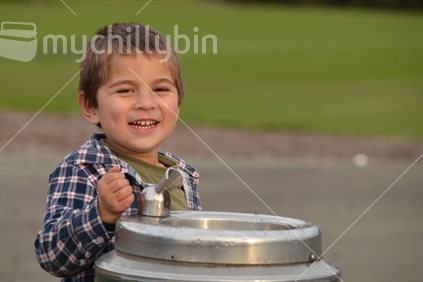 A young boy smiles near a drinking fountain