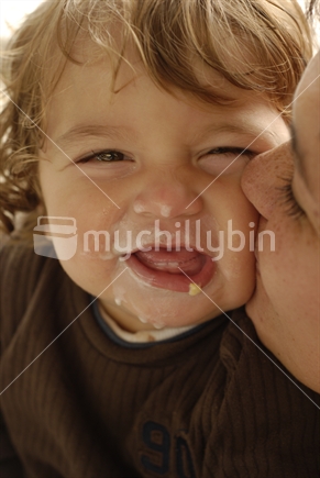 A giggling baby being kissed by his mother