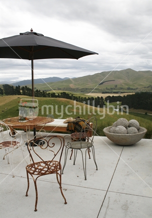 Black umbrella and antique table setting on a stone patio with a rural southern view