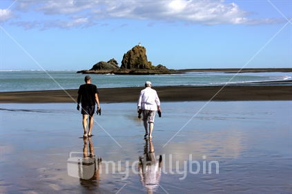Couple walking barefoot at Whatipu Beach, Auckland West, New Zealand.