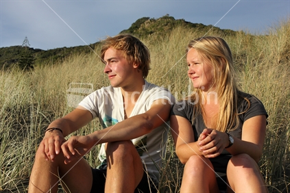 Two young people sitting in the sand dunes, Piha Beach, West coast
