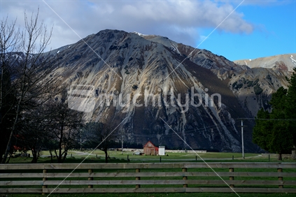 Steep scree slopes, wooden fence, and red roofed building at Lake Pearson, Canterbury, New Zealand.