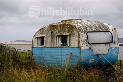 Old mouldy caravan by the seaside, reminiscent of years gone by; wired down to stop wind movement. 