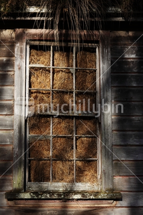 Old building stuffed with hay seen through broken window frame