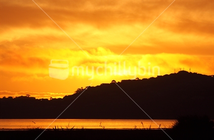 Orange sky showing in water, with silhouetted hills, New Zealand