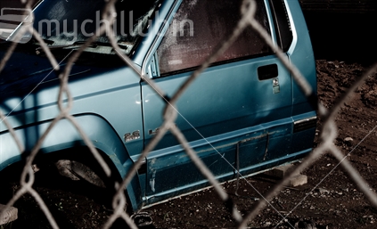 The wreck of a ute behind a fence