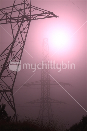 Sun shining through mist silhouetting 2 power pylons