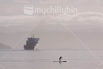 Ferry boat departing Wellington on a still, calm morning, with a paddleboarder in the foreground