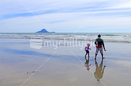 A father and daughter on the beach at Ohope, Whale Island in the background
