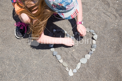 A young girl makes a heart in the sand