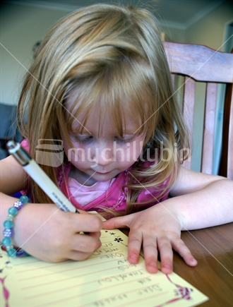 A young girl carefully writes a letter (face in focus)