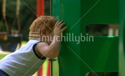 A little boy peeking into playground equipment