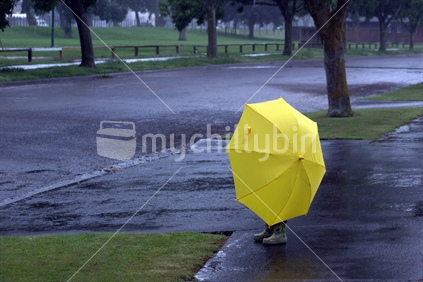 A child waiting under an umbrella on a stormy day