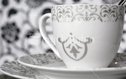 Fleur-de-lis design white teacup sits atop dinnerware