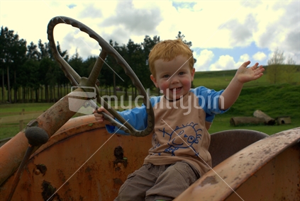 Young boy sitting on an old tractor, waving