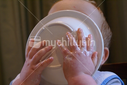A toddler happily licks his bowl clean
