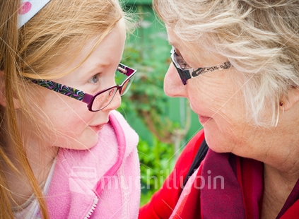 A Granddaughter poses with her Nana, trying on her glasses.  