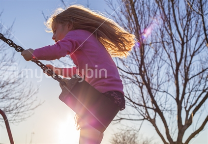 A young girl plays on the swing (backlit, solar flare)