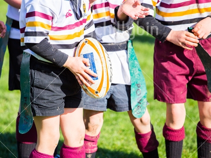 A young player holds the rugby ball mid-game