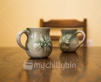 A pair of retro pottery mugs on an wooden dining table 