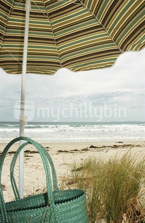 Beach umbrella and woven bag on beach, Coromandel, New Zealand
