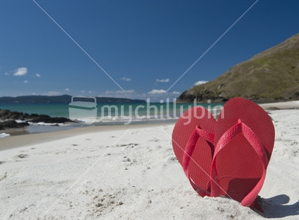 Heart shape made by red jandals on a beach.
