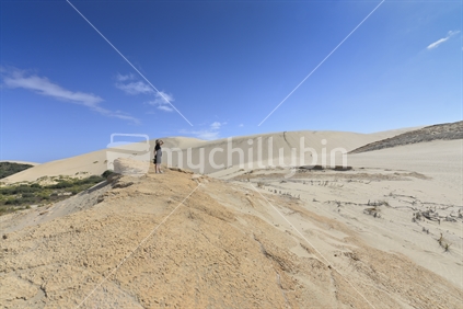 Young woman looking at distant people at top of dune. Giant sand dunes, 90 Mile beach, Te Paki