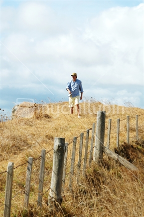 Man walking on farmland next to barbed wire fence