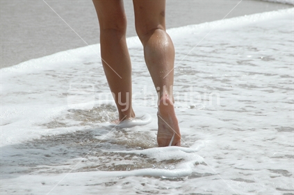 Bare legs and feet walking through water at beach