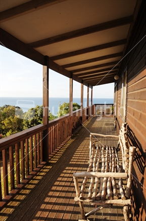 Long verandah with rustic seat made of sticks, with view of sea, New Zealand