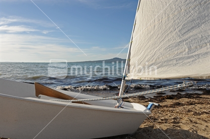 Close up of Optimist yacht with white sail on beach, New Zealand