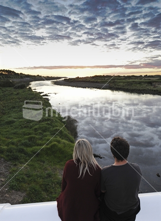 Couple watching sunset, sitting on a bridge