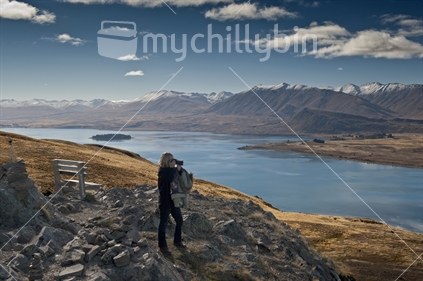 Woman taking photo from scenic viewpoint, Lake Tekapo.