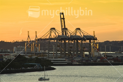 Auckland harbour and container cranes at sunset, orange sky.
