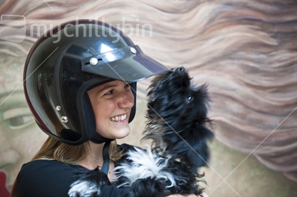 Young woman wearing safety helmet and cuddling a moving dog.