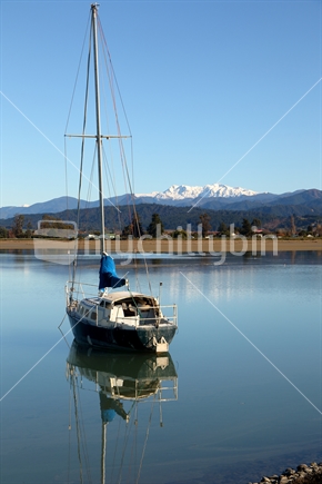 Yacht in harbour at Motueka Port with snow-covered Mount Arthur in background.