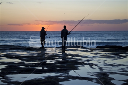 Two men fishing at sunset off the rocks at Muriwai, New Zealand