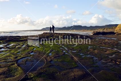 A man and a boy taking in the view from the rocks at Muriwai on the West Coast, New Zealand