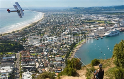 Girl on Mt Maunganui observing a Tiger Moth bi-plane, cruise liner, and the Mt Maunganui community. 