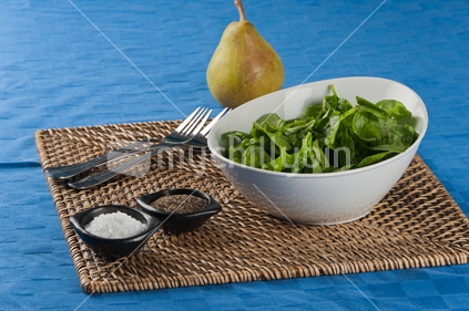 Spinach salad, with pea on blue tablecloth.