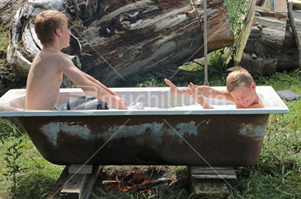 Two boys splashing in an out door old bath