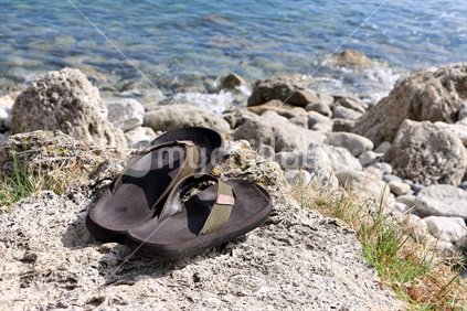 Jandals on the rocky shore with clear clean water in the background