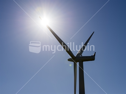The windfarms near Wellington on the west coast at Makara, the pylons stand tall among green farmland and grazing sheep, generating power for Wellington and New Zealand. A single turbine with one blade in front of the sun