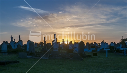 Grave markers at the Waipu cemetery silhouetted by the setting sun heralding death or change or the final rest